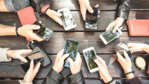 Manos de jóvenes sosteniendo móviles sobre una mesa de madera